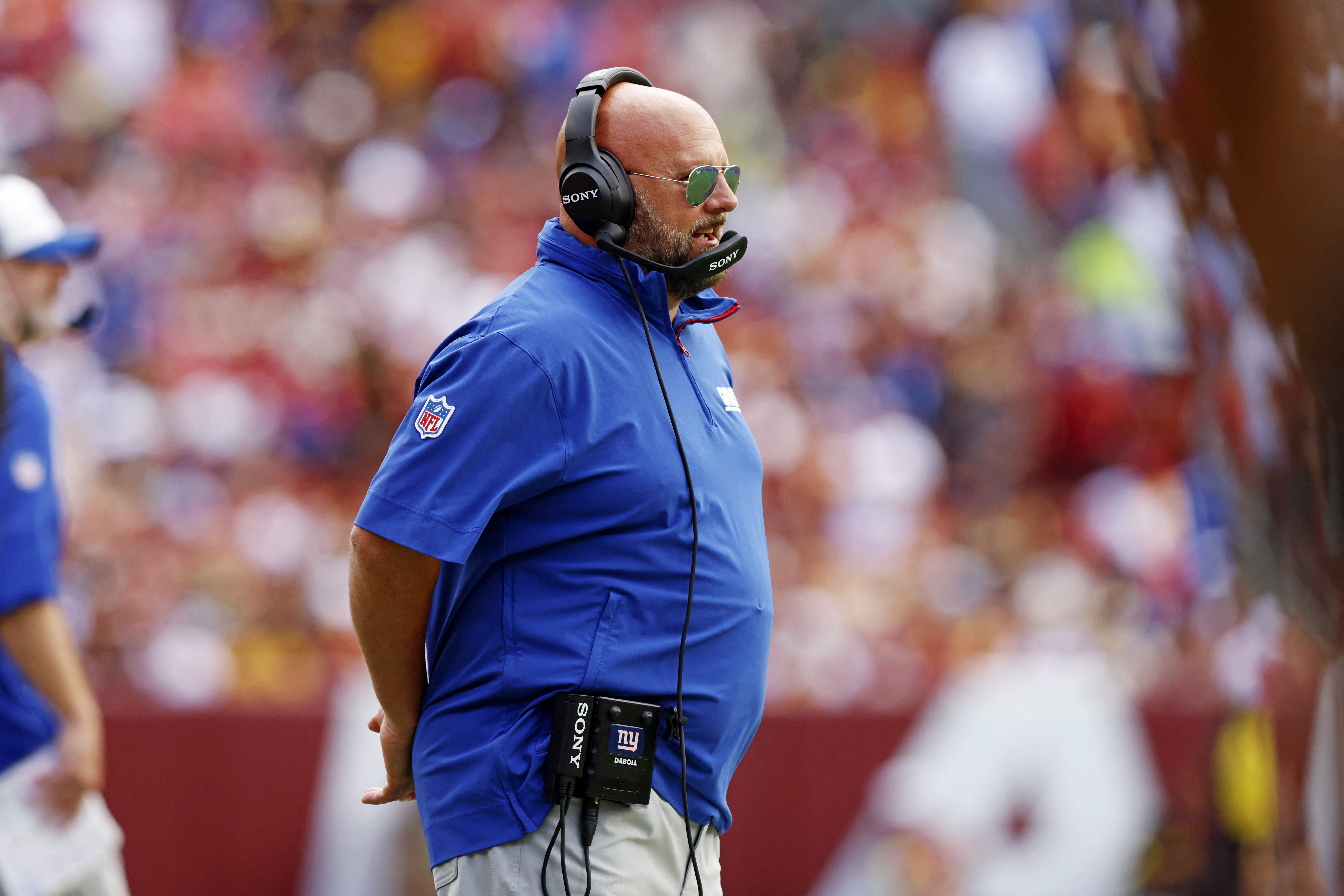 Brian Daboll: Giants head coach in blue shirt stands with hands behind back inside football stadium