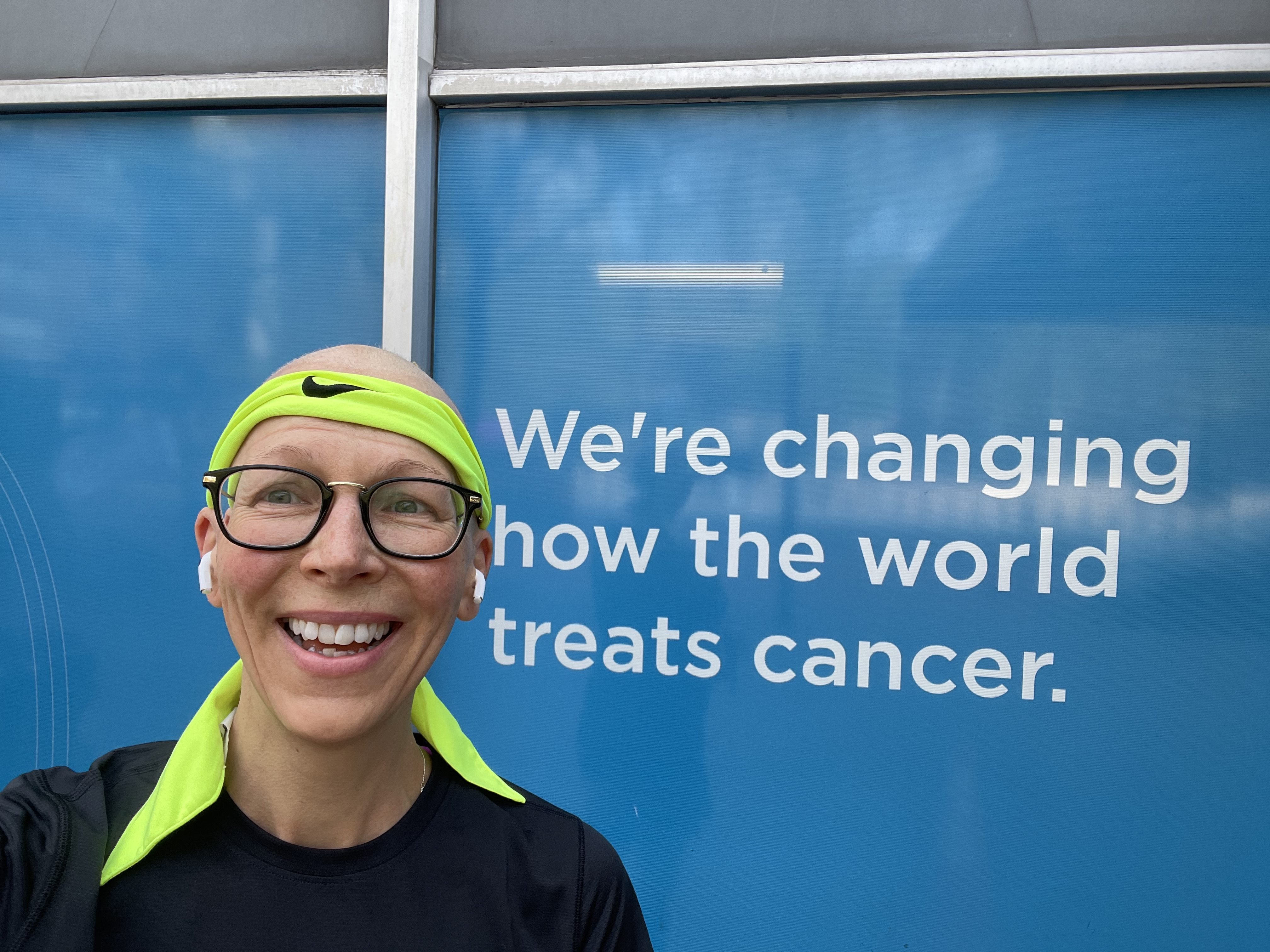 Pauline Larkin in front of a sign that reads "we're changing how the world treats cancer"
