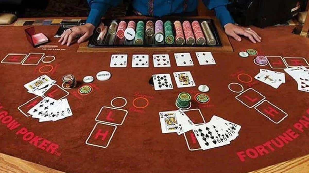 An overhead view of a Pai Gow Poker table in a casino, showing players arranging their cards into a five-card hand and a two-card hand. The table is covered with a green felt surface, displaying card rankings and game instructions